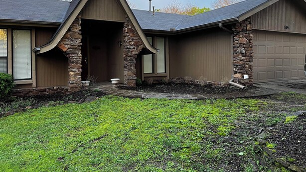 A house with a stone facade, a garage, and a front yard with grass and mulch. - Serene 3-bedroom house with AC in charming Fort Smith (Fort Smith)