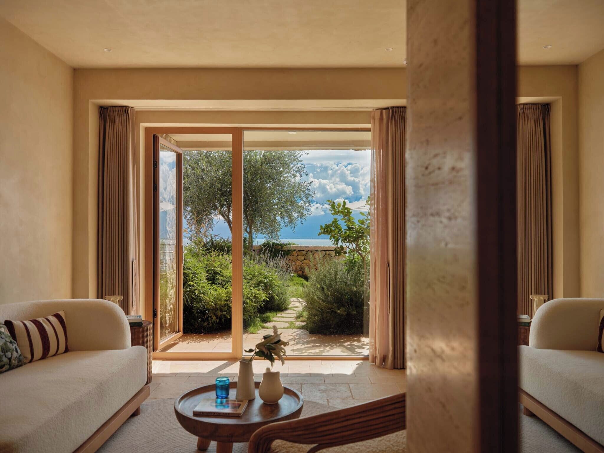 Una habitación con sofá, una mesita de centro y vistas a un jardín y al mar.