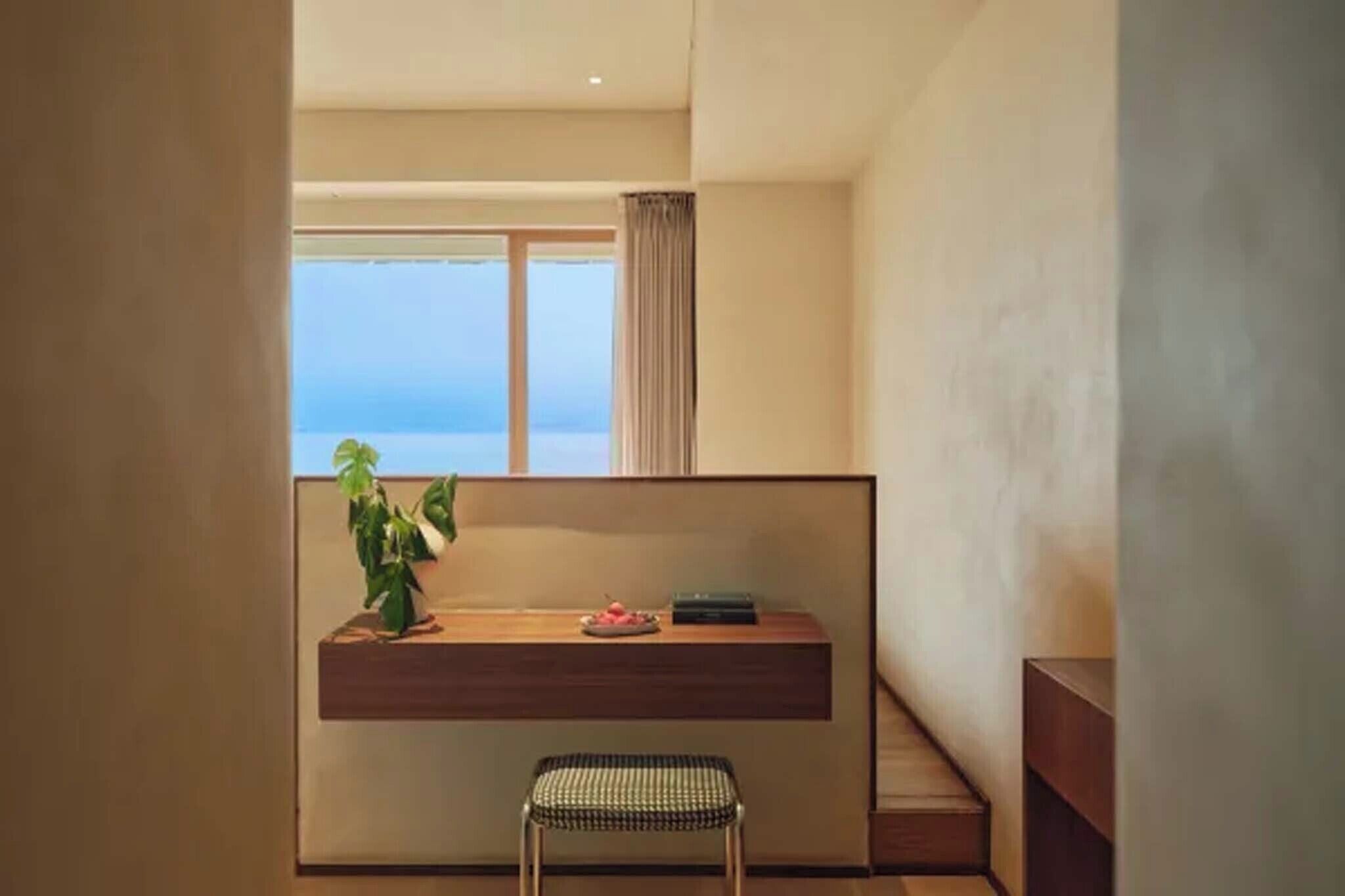 A modern room with a wooden desk, a potted plant, and a view of the sea.