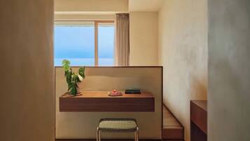 A modern room with a wooden desk, a potted plant, and a view of the sea.