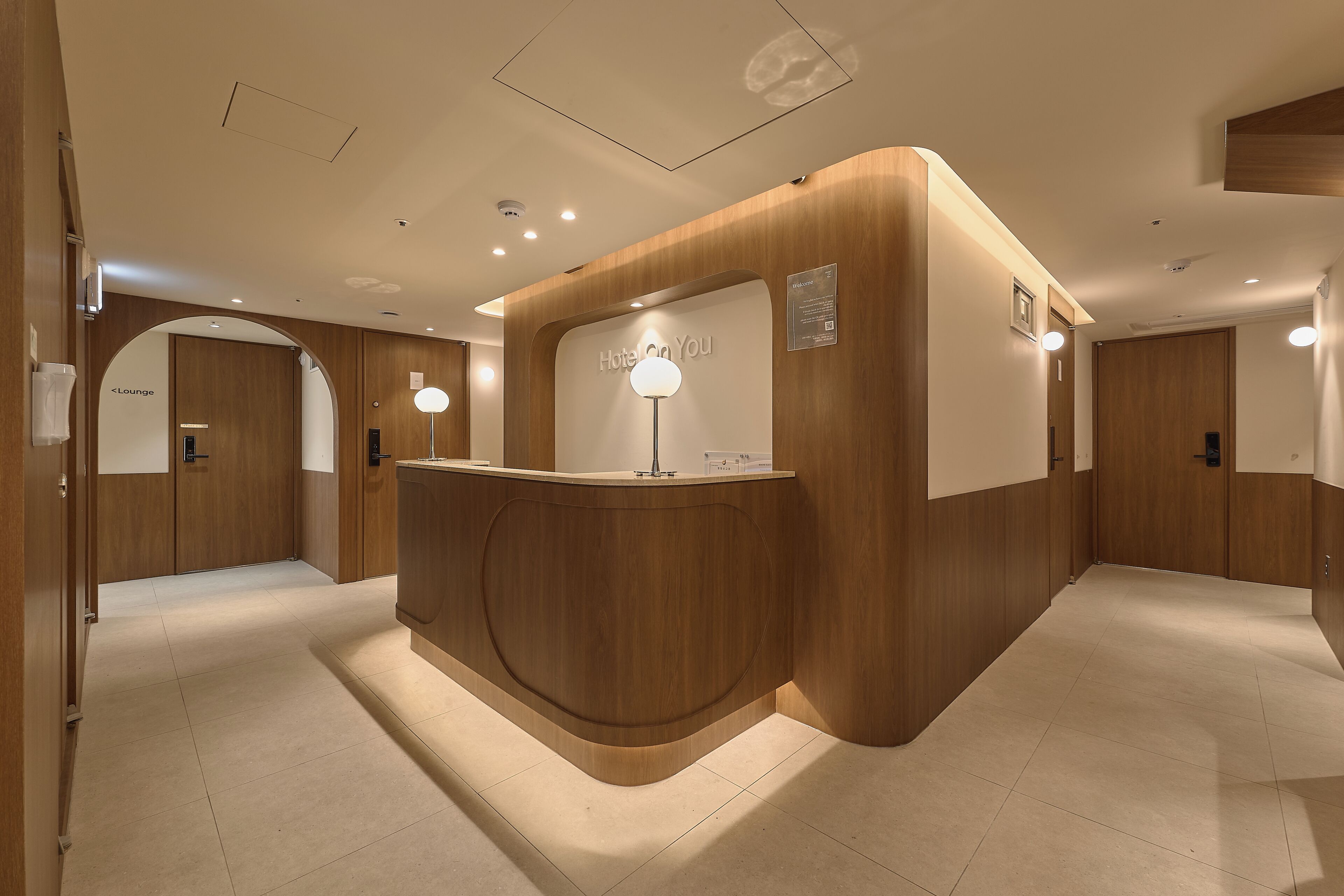 Een receptiebalie met een 'Hotel on You' bord, houten lambrisering en een 'Lounge' bord op de achtergrond.