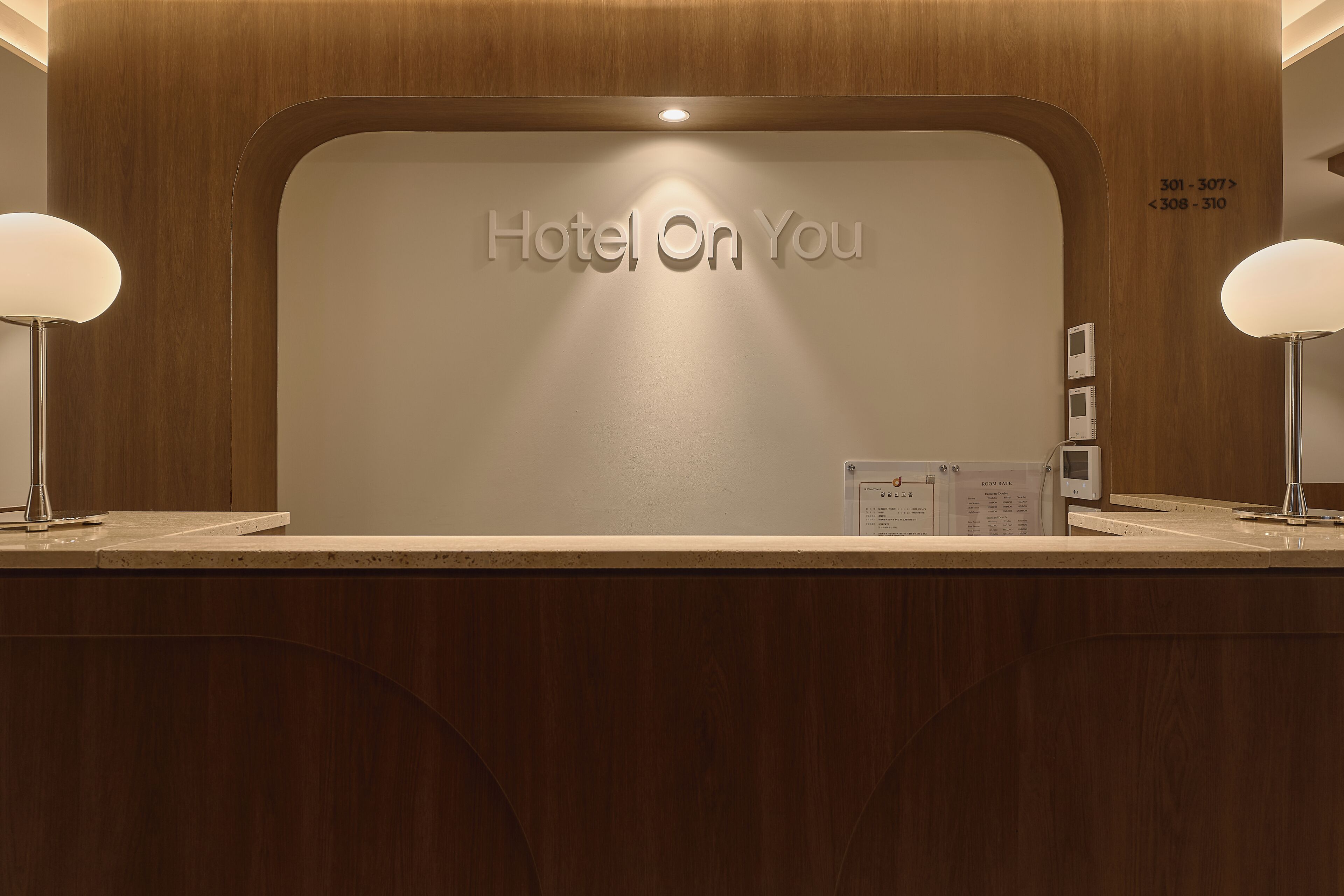 A hotel reception desk with a 'Hotel On You' sign, a wooden panel design, and a reception counter.
