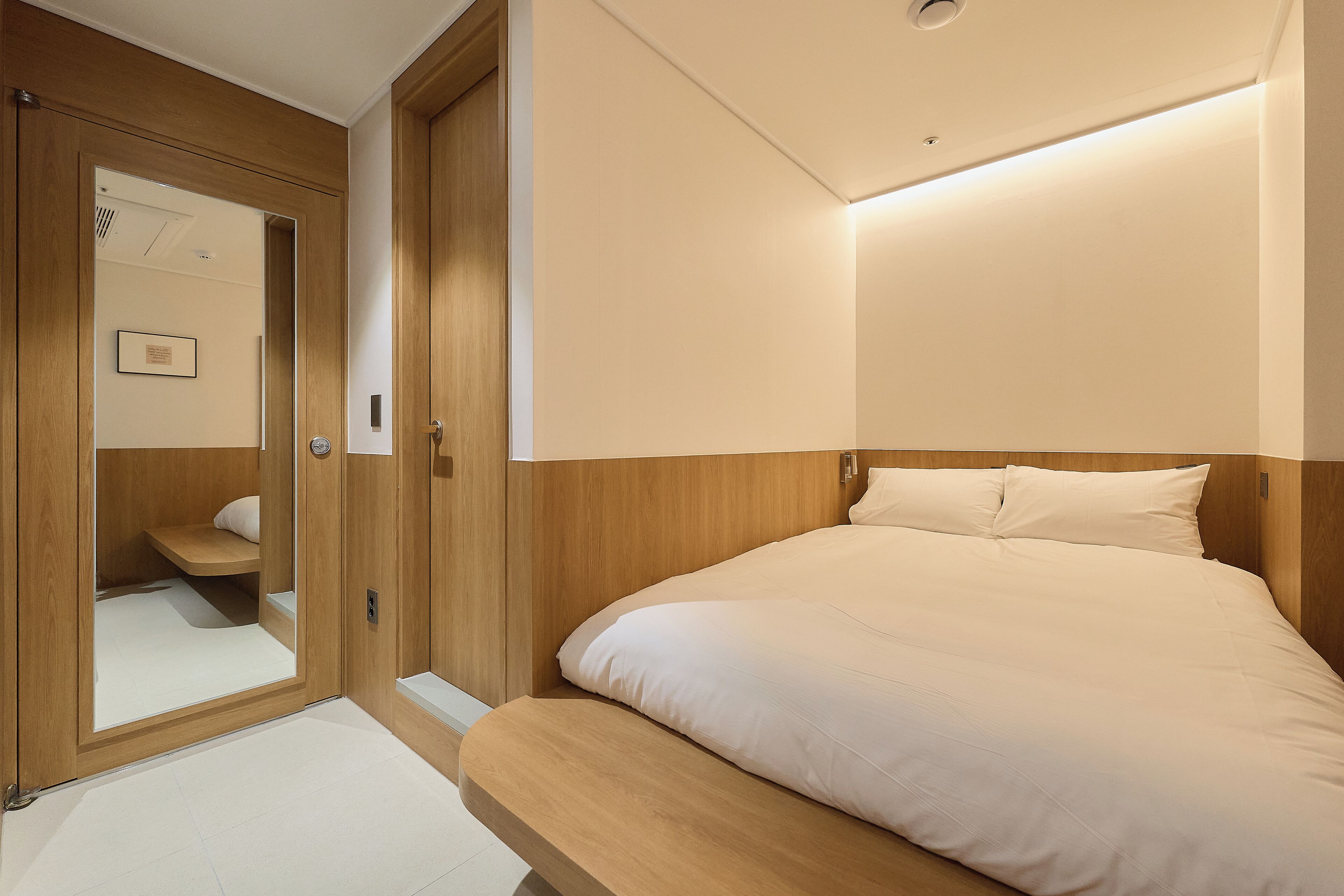 A bedroom with a wooden headboard, a bed with white bedding, a wooden wardrobe, and a mirror.