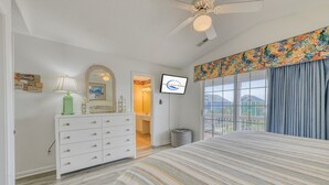 Un dormitorio con cama, cómoda, tocador, ventilador de techo, televisor y balcón con cortinas.