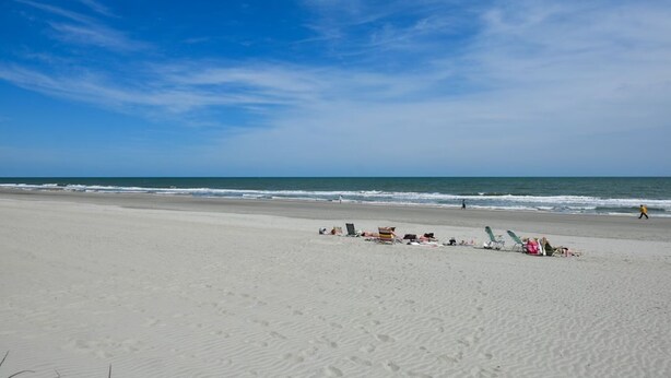 Una extensa playa de arena con cielo azul despejado y mar tranquilo.