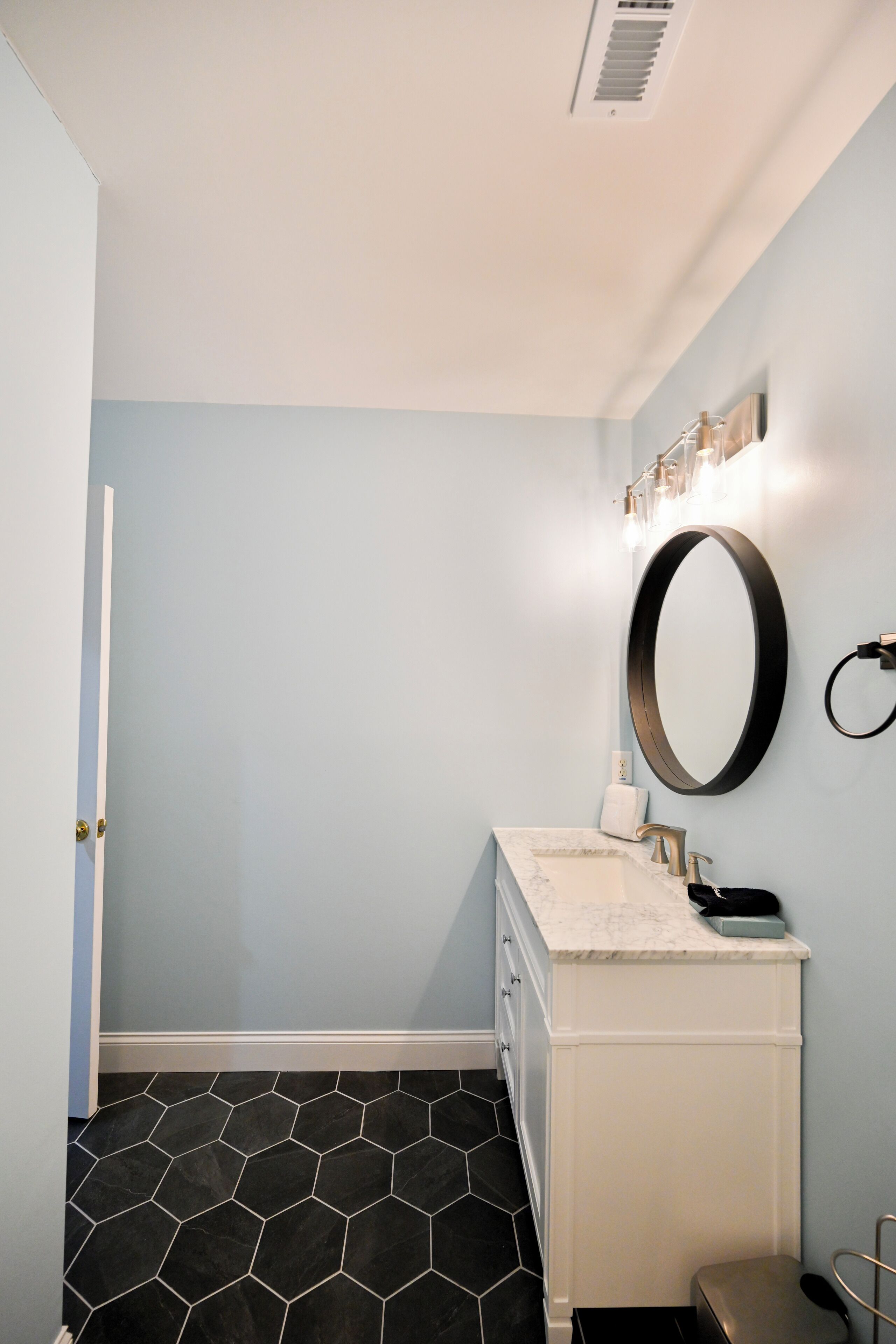 Un baño con tocador blanco, suelo de baldosas hexagonales negras y pared azul claro.