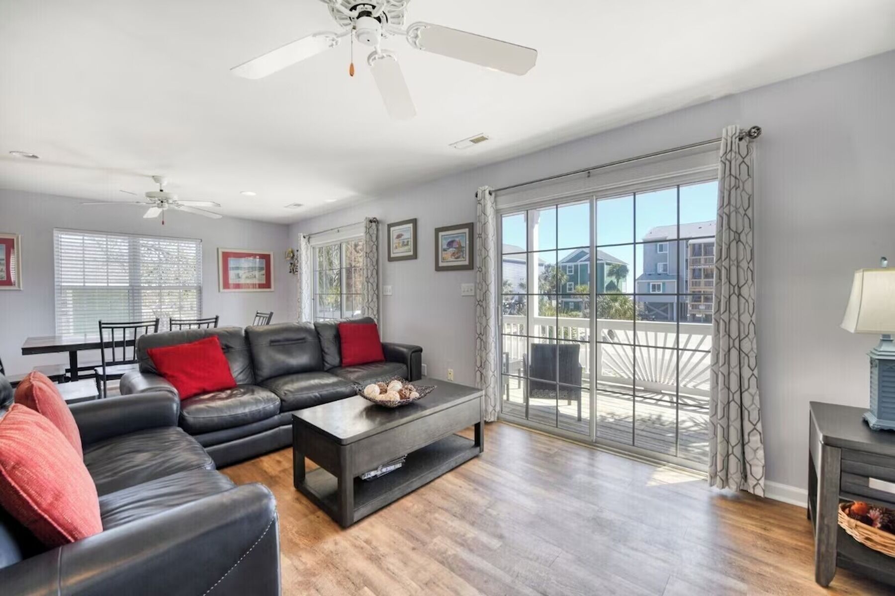 Un vaste salon comprenant un canapé en cuir noir, une table basse et un coin repas avec une table et des chaises. Un balcon offre une vue sur le quartier.