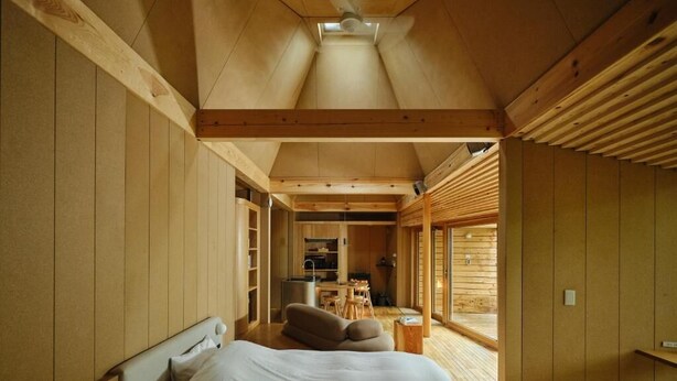Een slaapkamer met een bed, een bank en een kleine tafel. Een keuken is zichtbaar door een geopende deur.