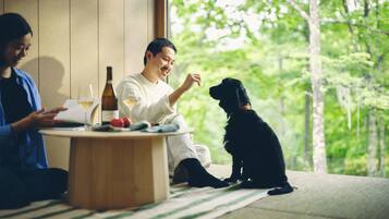A room with a large window, a round wooden table, and a black dog sitting on a striped mat.