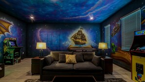 A room with a starry ceiling, a ship mural, arcade games, a couch, and a bed. - 8 BR Resort Home with Pool, Hot Tub, Game Room and Theater - Near Disney (Kissimmee)