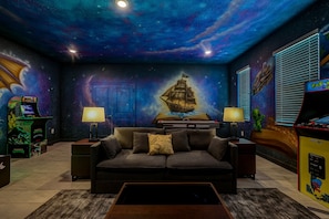 A room with a starry ceiling, a ship mural, arcade games, a couch, and a bed. - 8 BR Resort Home with Pool, Hot Tub, Game Room and Theater - Near Disney (Kissimmee)