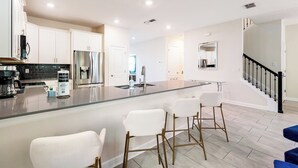 A modern kitchen with white cabinets, stainless steel appliances, and a central island with bar stools. - 8 BR Resort Home with Pool, Hot Tub, Game Room and Theater - Near Disney (Kissimmee)