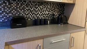 A kitchen with a toaster, coffee maker, and mugs on the counter. - 2 bedroom deluxe apartment in Leicester (Leicester)