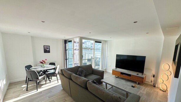 A modern living room with a sofa, TV, and dining area. - 2 bedroom deluxe apartment in Leicester (Leicester)