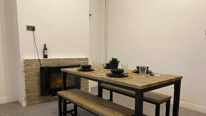 A dining area with a wooden table and benches, a small potted plant, and a fireplace. - Spacious 3 bedroom House in Sheffield (Handsworth)