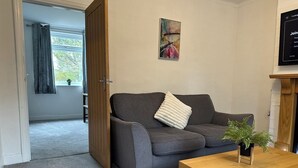 A living room with a grey sofa, a wooden coffee table, a painting on the wall, and a door leading to another room. - Spacious 3 bedroom House in Sheffield (Handsworth)