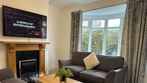 A living room with a fireplace, a television mounted above it, a sofa, a coffee table, and a window with curtains. - Spacious 3 bedroom House in Sheffield (Handsworth)