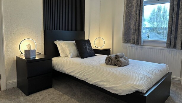 A modern bedroom with a bed, bedside tables, a window with curtains, and a radiator. - Spacious 3 bedroom House in Sheffield (Handsworth)