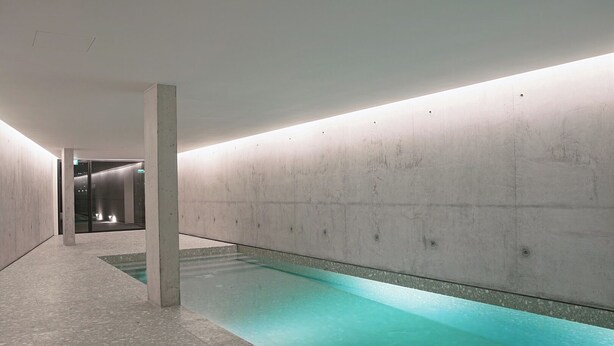 A modern indoor pool with a clear water surface, surrounded by concrete walls and a tiled floor. - Riverside Luxe 2BR | Pool, Spa, Balcony and Parking (Vila Nova de Gaia)
