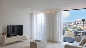 A modern living room with a flat-screen TV, a sofa, a coffee table, and a balcony with a table and chairs. - Riverside Luxe 2BR | Pool, Spa, Balcony and Parking (Vila Nova de Gaia)