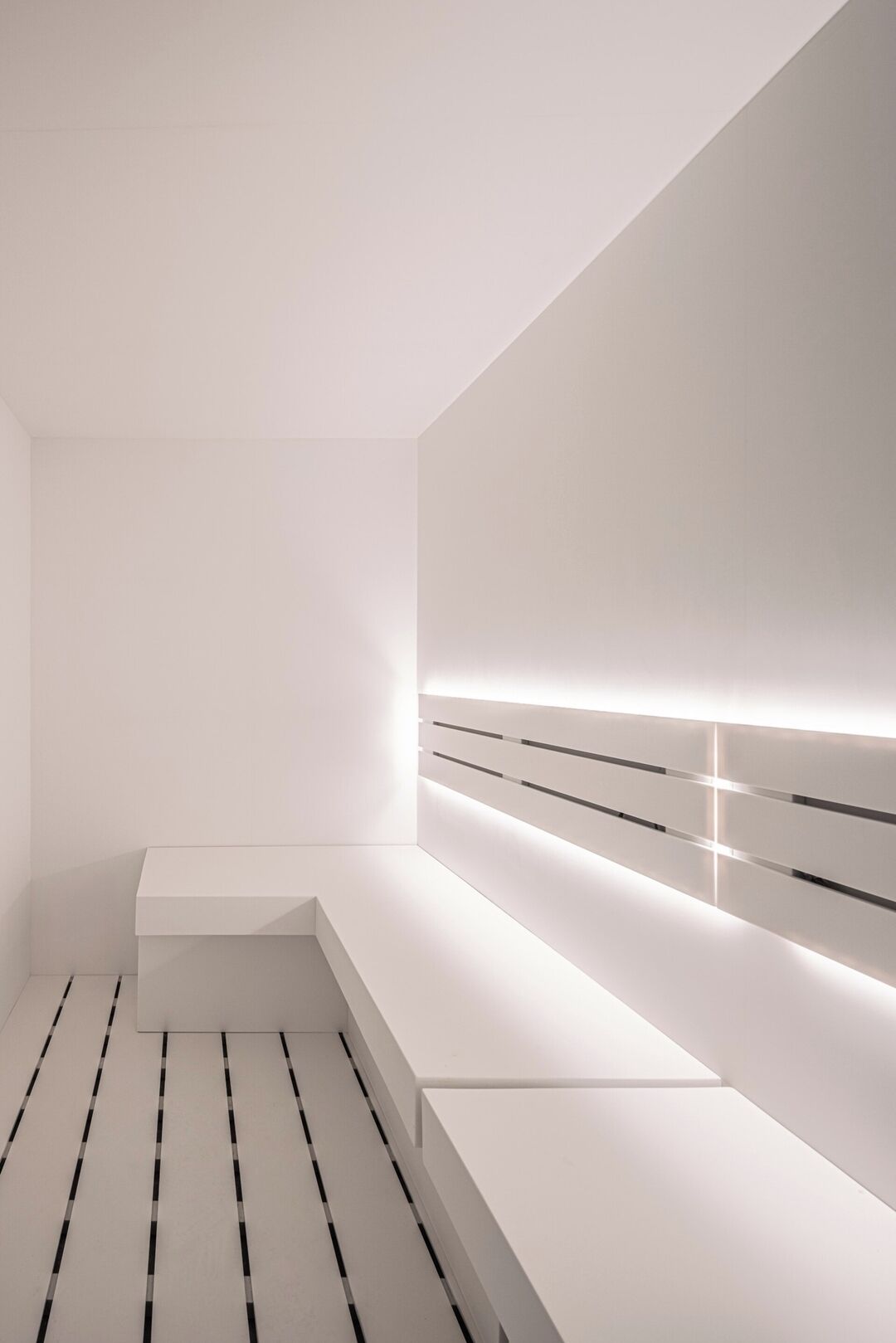A minimalist room with a white bench, a sloped ceiling, and a wall-mounted light strip.