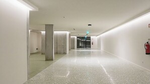 Um corredor comprido e estreito com piso lustroso, paredes brancas e um extintor de incêndio fixado na parede direita.