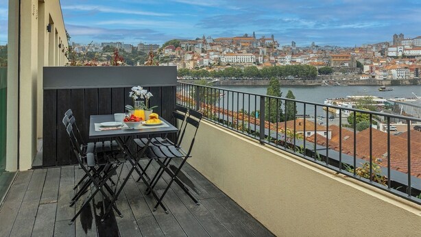 Varanda com mesa posta para café da manhã, vista para a paisagem urbana e rio.