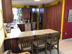 A kitchen with wooden cabinets, a granite countertop, a refrigerator, and a coffee maker. - A Private Paradise by the Rainforest in Sunny Luquillo (Pitahaya)