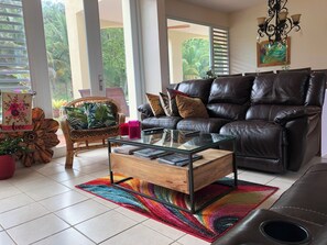 A living room with a leather sofa, a glass coffee table, a wicker chair, and a colorful rug. - A Private Paradise by the Rainforest in Sunny Luquillo (Pitahaya)