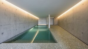 Ein langer, schmaler Innenpool mit gerader, schlichter Gestaltung, umgeben von schlichten Betonwänden und einer einfachen, unbeleuchteten Decke.