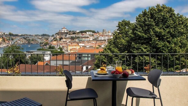 Ein Balkon mit einem für das Frühstück gedeckten Tisch, mit Blick auf eine Stadtlandschaft mit einer Brücke und historischen Gebäuden.