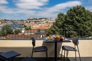A balcony with a table set for breakfast, overlooking a cityscape with a bridge and historic buildings. - Design T2 Duplex Pool and Balcony (Vila Nova de Gaia)