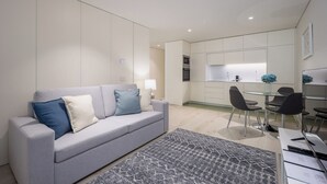 Een moderne woonkamer met een grijze bank, een tapijtend en een eethoek met een glazen tafel en stoelen.