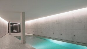 A modern indoor pool with a clear water surface, surrounded by concrete walls and a tiled floor. - Porto Glam River View and Spa (Vila Nova de Gaia)