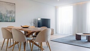 A modern living room with a dining area, featuring a large flat-screen TV, a dining table with six chairs, and a coffee table. - Porto Glam River View and Spa (Vila Nova de Gaia)