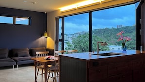 Una cocina moderna con una isla grande, un comedor con mesa y sillas, y vistas a un paisaje urbano a través de amplios ventanales.