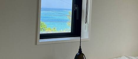 A room with a window overlooking a beach, a bed with white bedding, and a hanging lamp.