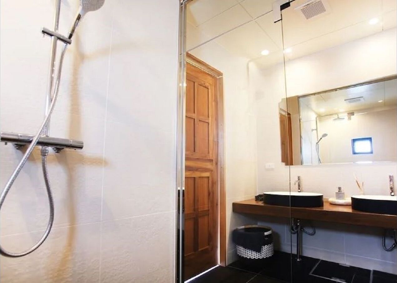 Et moderne badeværelse med et glasbadeværelsesafskærmning, en trädør og et håndvaskbord med to håndvaske og et spejl.