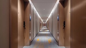 Un long couloir étroit, avec des portes en bois de chaque côté, un éclairage encastré et une moquette à motifs.