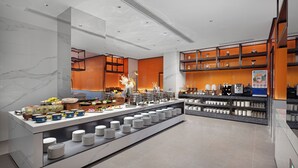 Un hall d’hôtel moderne doté d’un espace buffet proposant une variété de plats et de boissons, d’un sol en marbre et d’une décoration contemporaine.