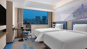 Une chambre d’hôtel avec deux lits, un bureau, une chaise, une télévision et une grande fenêtre donnant sur la ville.