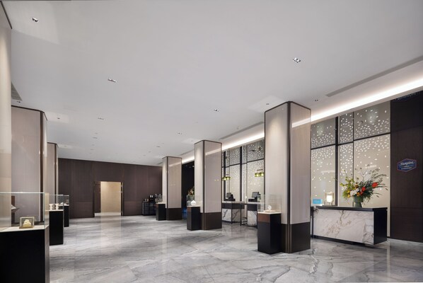 A modern hotel lobby with marble flooring, a reception desk, and a large window with decorative elements.