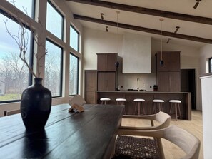 A modern kitchen with large windows, wooden beams, and a central island with stools.