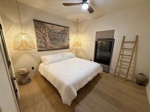 Quarto com cama, duas luminárias na parede, escada, porta e um quadro na parede.
