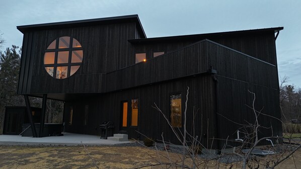 A modern two-story house with a large circular window on the upper floor and a covered outdoor area.
