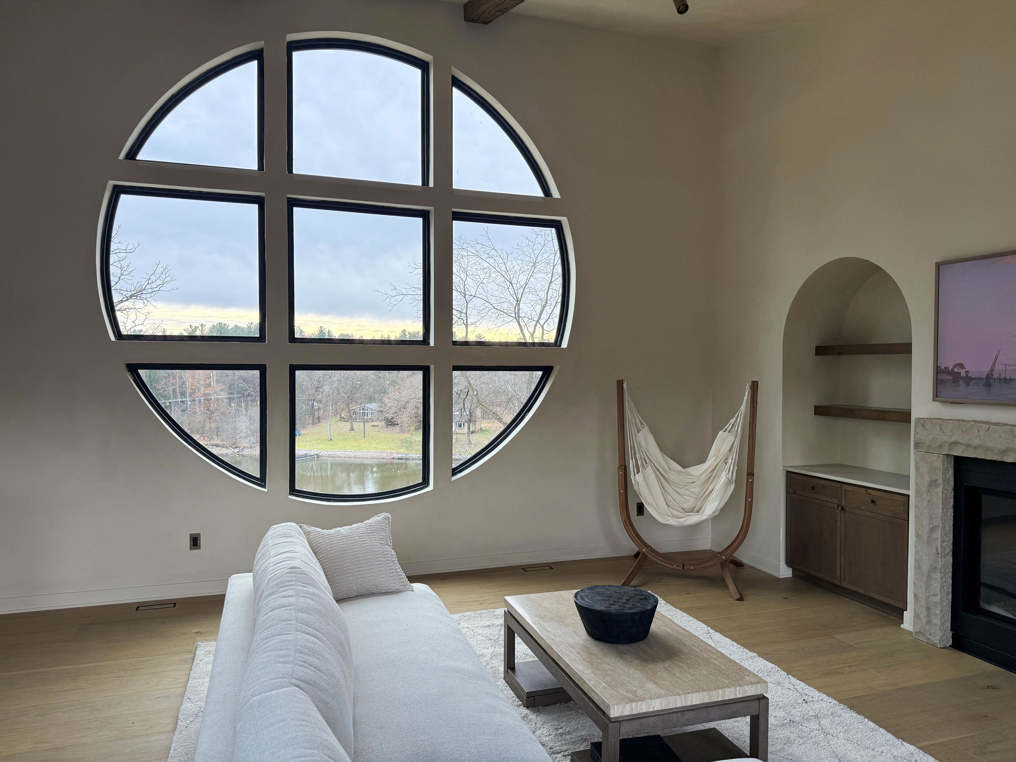 A modern living room with a large circular window, a hammock, a fireplace, and a sofa.