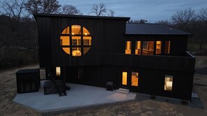 A modern two-story house with a large circular window on the front, multiple windows on the upper floor, and a patio area with outdoor furniture.