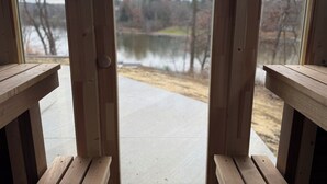 A wooden deck with benches overlooking a lake and trees. - The Overhang · Luxury River Retreat with Sauna, Hot Tub, Movie Theater, & Arcade (Janesville)