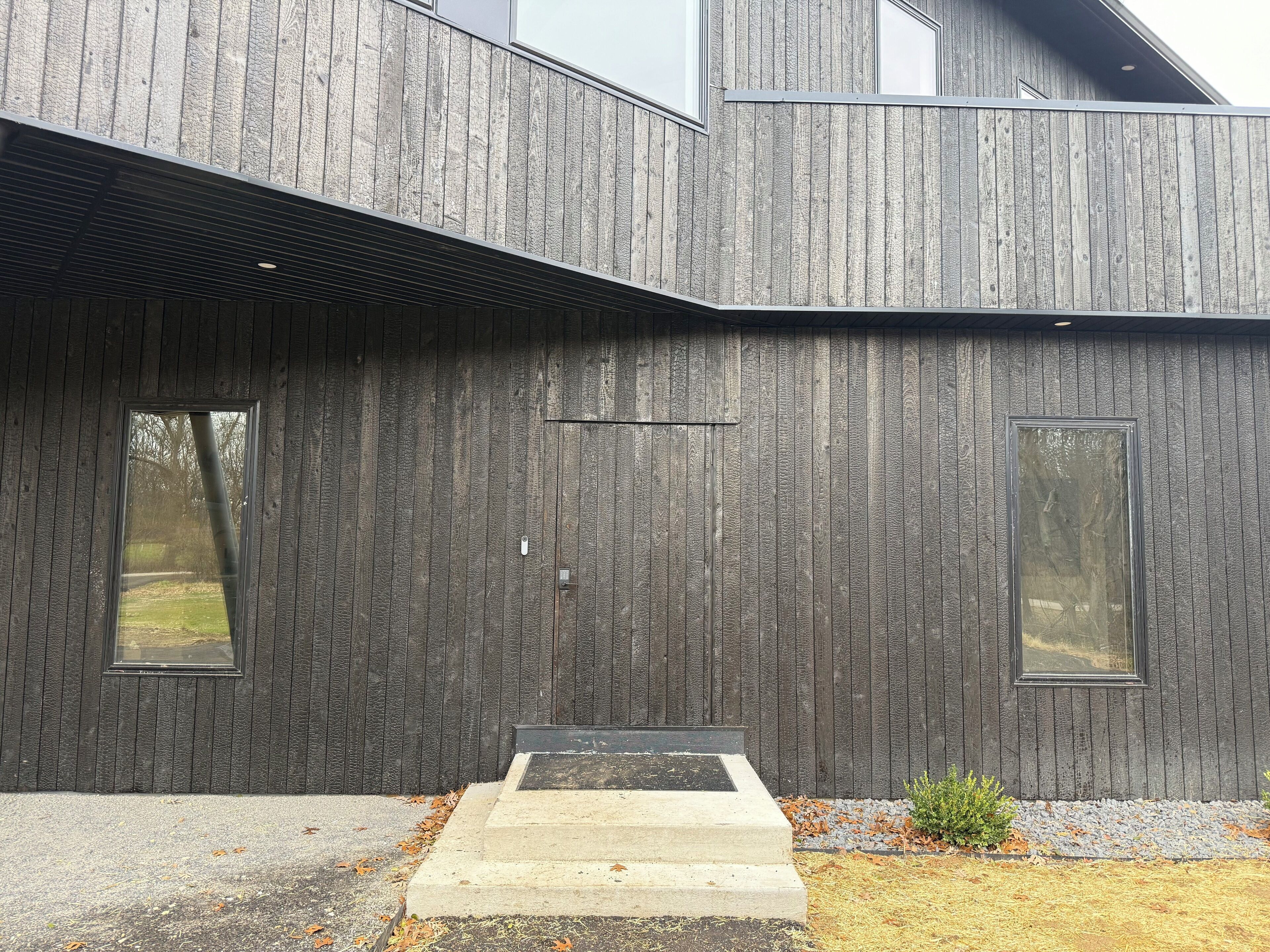 A modern building with a dark wooden exterior, large windows, and a concrete entrance.