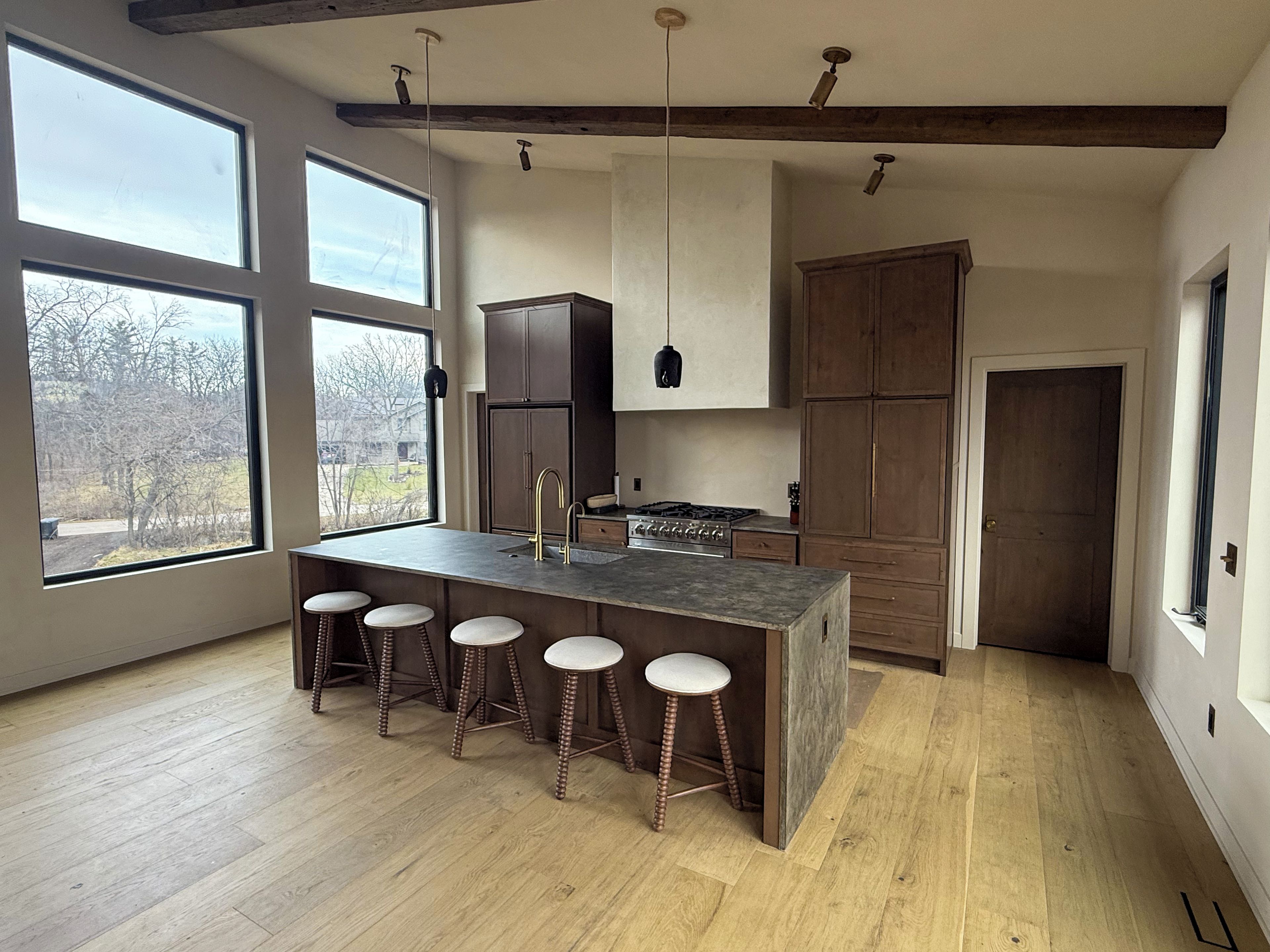 A modern kitchen with a central island, bar stools, and large windows.